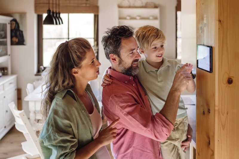 Family looking at smart thermostat adjusting lowering heating temperature at home Concept of sustainable efficient and smart technology in home heating and thermostats | WilkComm Reno